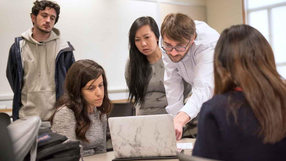 A professor demonstrating to a group of student with a computer